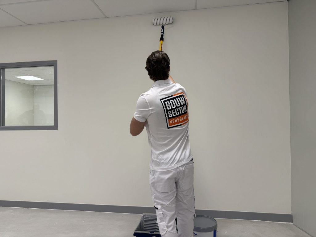 Schilder rolt een witte muur tot vlak onder het plafond met een roller aan een steel