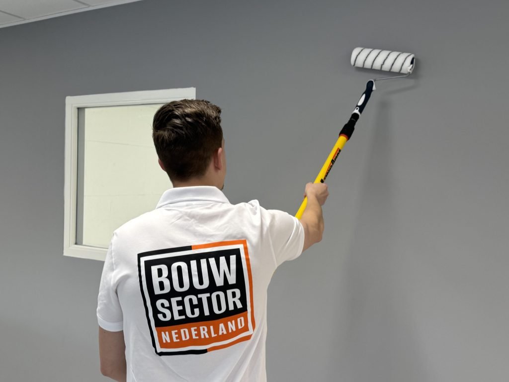Schilder met Bouwsector Nederland-polo zet een grijze muur in de verf met een roller op een steel