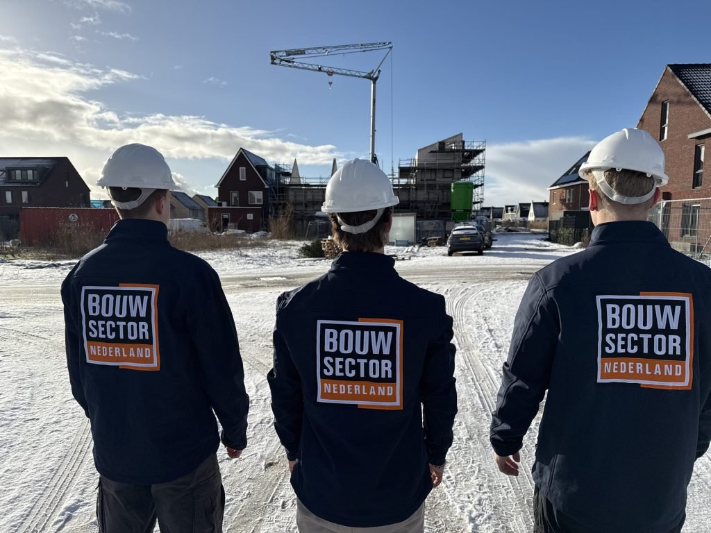 Drie vakmensen van Bouwsector Nederland met witte helm kijken naar huizen in aanbouw in de sneeuw
