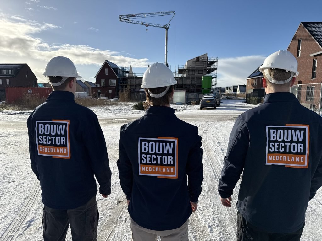Drie medewerkers van Bouwsector Nederland in jas met logo lopen over een besneeuwde straat naar nieuwbouwhuizen